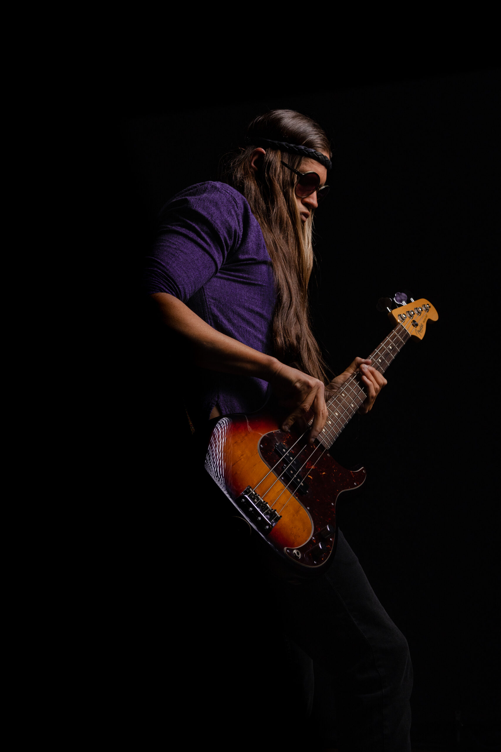 Drew Cornick holding a Fender Precision Bass in front of a dark background with a single light cast across face, body, and instrument as a Portrait example in Orange County.
